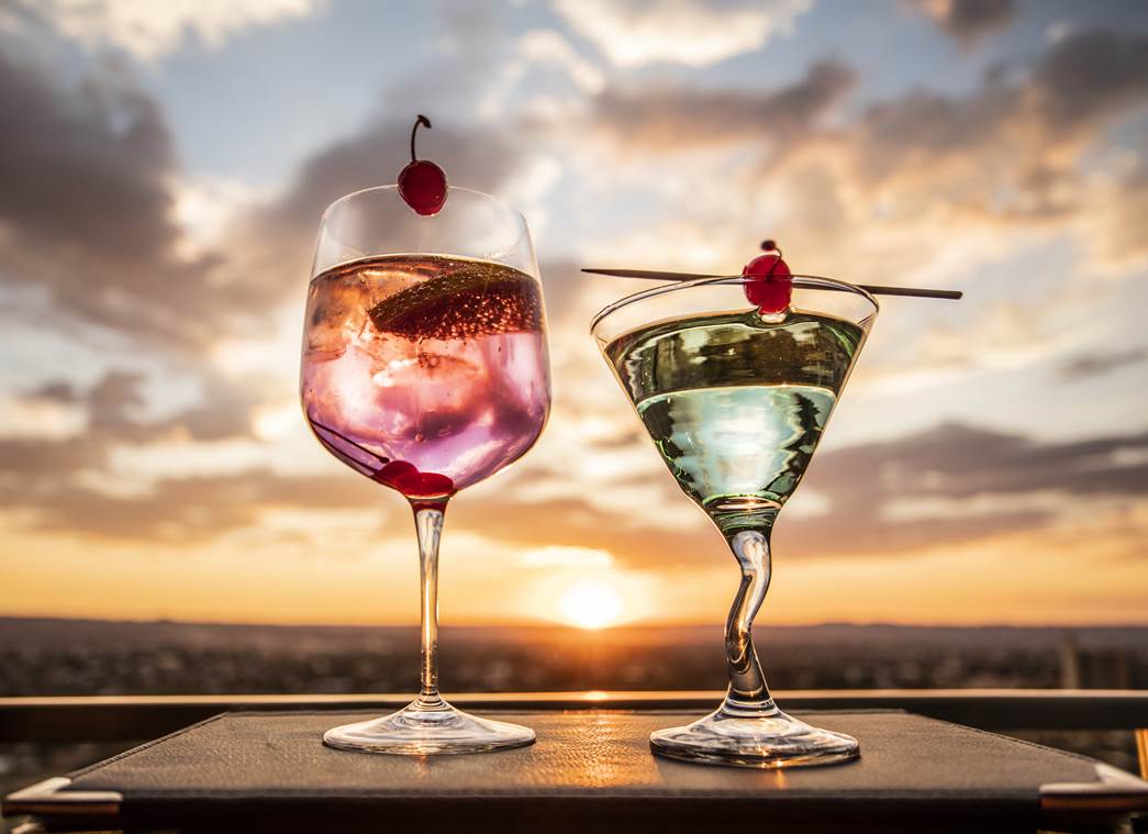 Two cocktails set against a sunset backdrop.