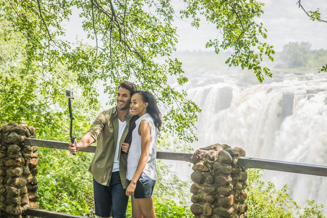 A couple with a selfie stick taking photos in front of the Victoria Falls.