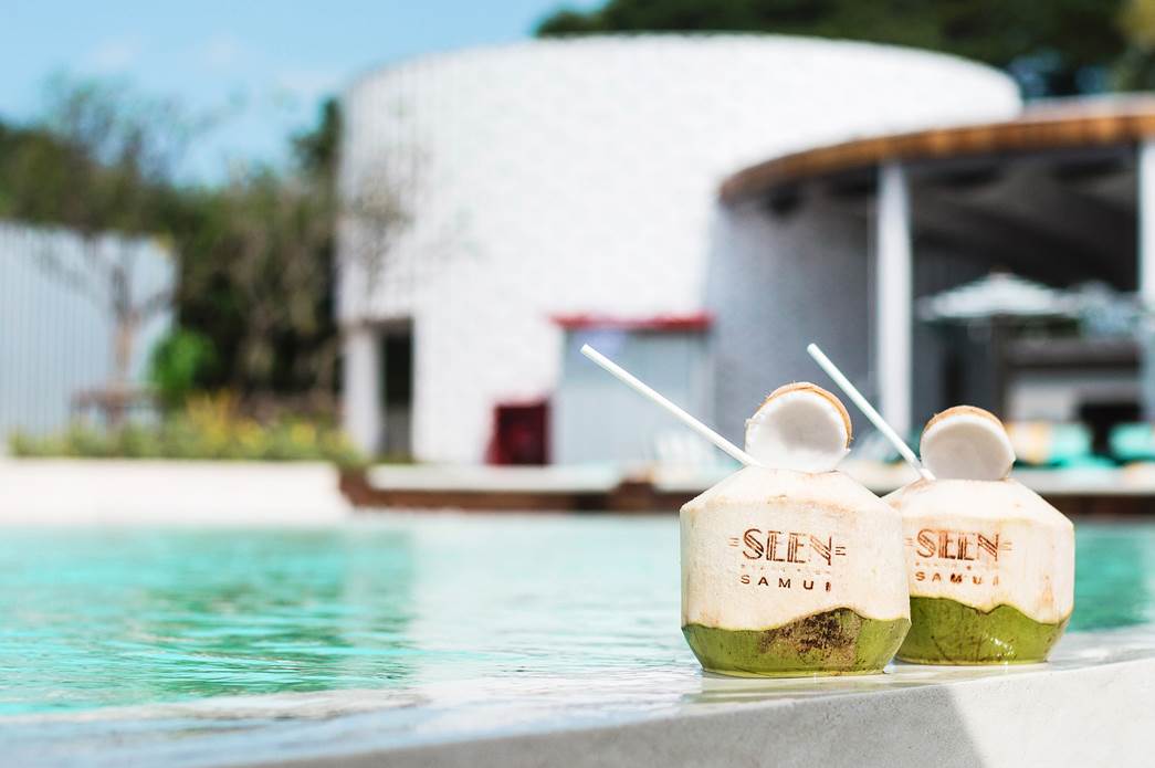 Two coconuts with "SEEN Beach Club Samui" inscribed sitting by the swimming pool.